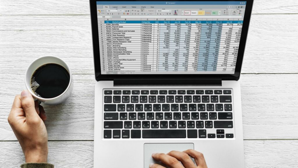 Tabelle auf Bildschirm eines Macbooks, Hände und Kaffeetasse: Symbolbild für einen Geschäftsführer und Weiterbeschäftigung