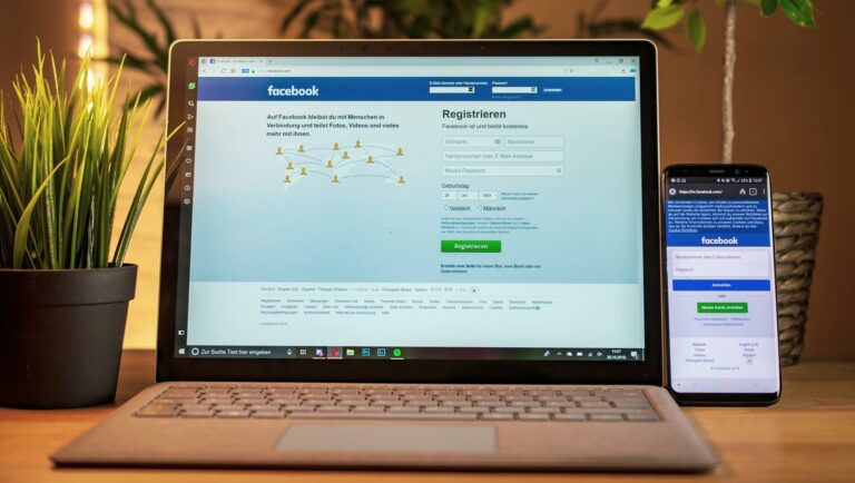 Tisch mit Blumentopf, Laptop und Handy mit Facebook-Login - Symbolbild für Facebook Impressumspflicht