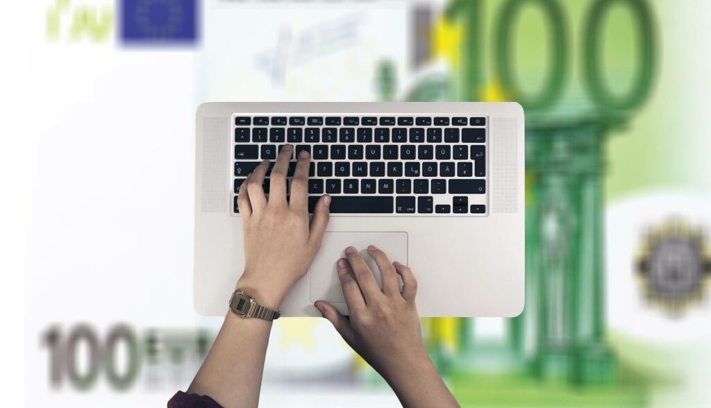 Hände auf Tastatur, Hintergrund: 100,- Euro-Scheine