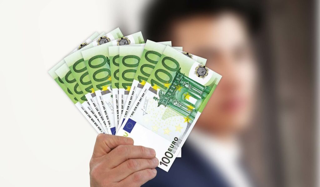 Person mit mehreren gefächerten 100 EUR-Scheinen in der Hand