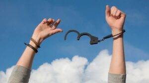 zwei Arme mit offenen Handschellen hoch gestreckt vor blauem Himmel